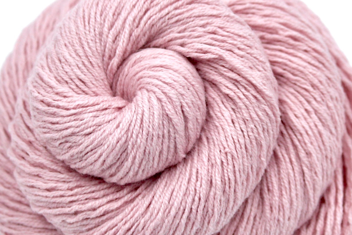 A close up shot of a skein of Vegan, Light Ballet Pink, Cotton/ Acrylic, Sport weight Yarn recycled by hand from unwanted sweaters beautifully coiled in the center of the frame.