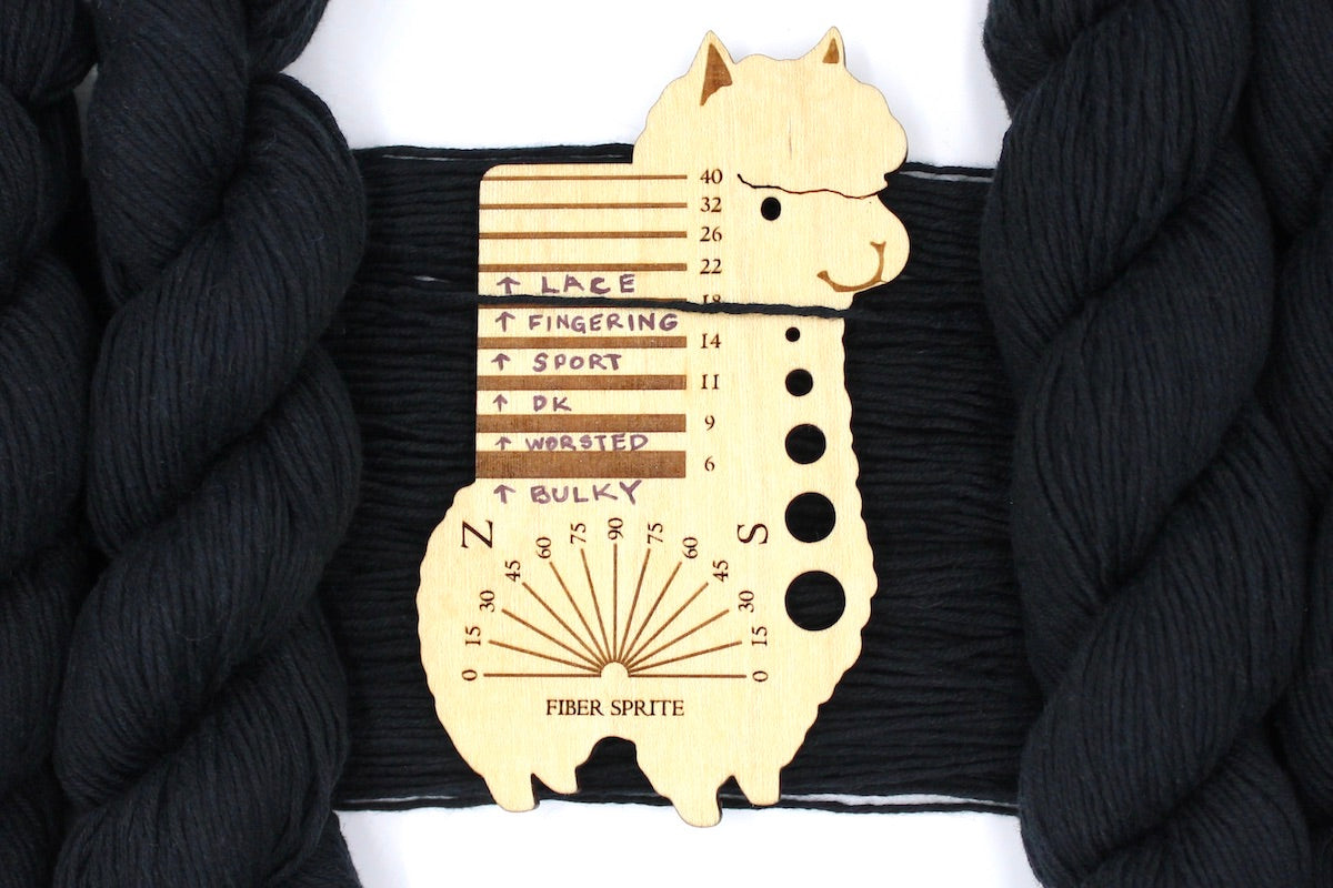 A skein of Vegan, Black, 100% Cotton, Fingering Weight Yarn recycled by hand from unwanted sweaters draped over a Llama shaped Yarn weight tool.