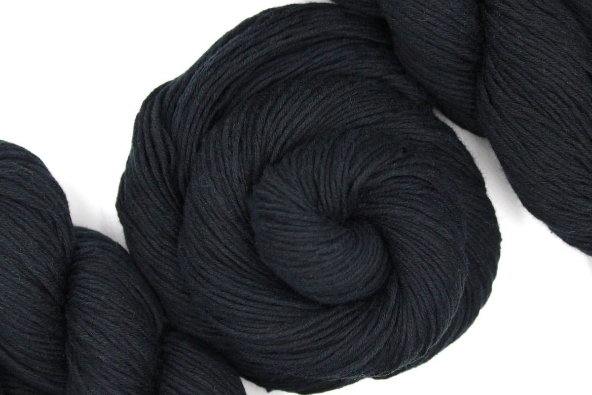 A skein of Vegan, Black, 100% Cotton, Fingering weight Yarn recycled by hand from unwanted sweaters swirled attractively in the center of the frame.