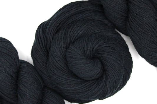 A skein of Vegan, Black, 100% Cotton, Fingering weight Yarn recycled by hand from unwanted sweaters swirled attractively in the center of the frame.
