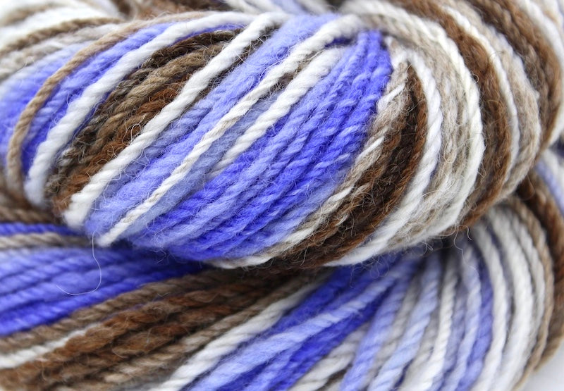 A close up view of a one of a kind, hand dyed Variegated skein of multicolored Purple, Lavender, White, Tan, and Brown self-striping wool Yarn.
