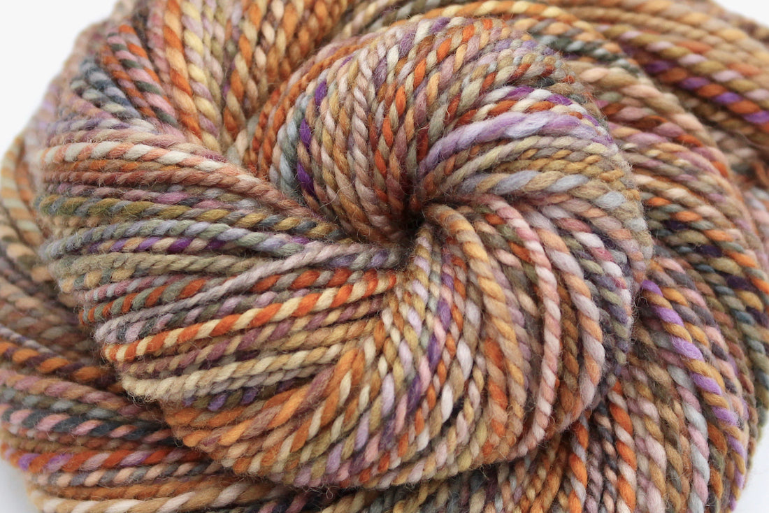 A close up view of a one of a kind, Worsted Weight, hand dyed variegated skein of multicolored Orange, Yellow, Pink, Purple, Olive Green, and Blue self-striping wool Yarn.