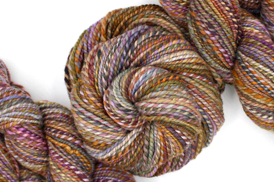 A one of a kind, Worsted Weight, hand dyed variegated skein of multicolored Orange, Yellow, Pink, Purple, Olive Green, and Blue, self-striping wool Yarn coiled attractively in the center of the frame.