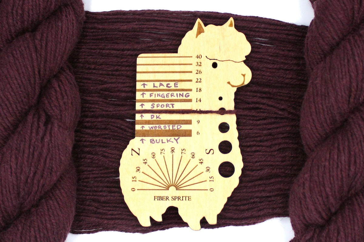 A skein of Vegan, Maroon/ Reddish Brown, Cotton/ Acrylic/ Nylon, Dk Weight Yarn recycled by hand from unwanted sweaters draped over a Llama shaped Yarn weight tool.