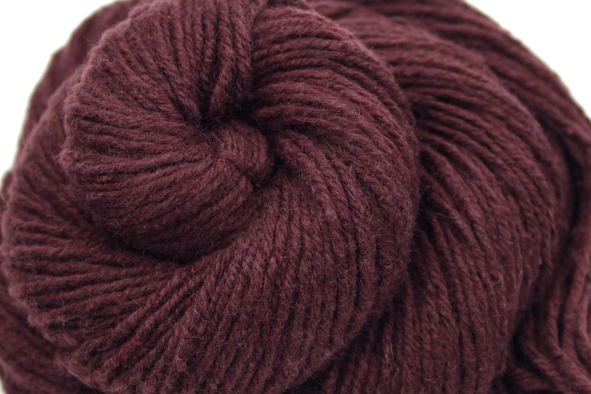 A close up shot of a skein of Vegan, Maroon/ Reddish Brown, Cotton/ Acrylic/ Nylon, Dk weight Yarn recycled by hand from unwanted sweaters beautifully coiled in the center of the frame.