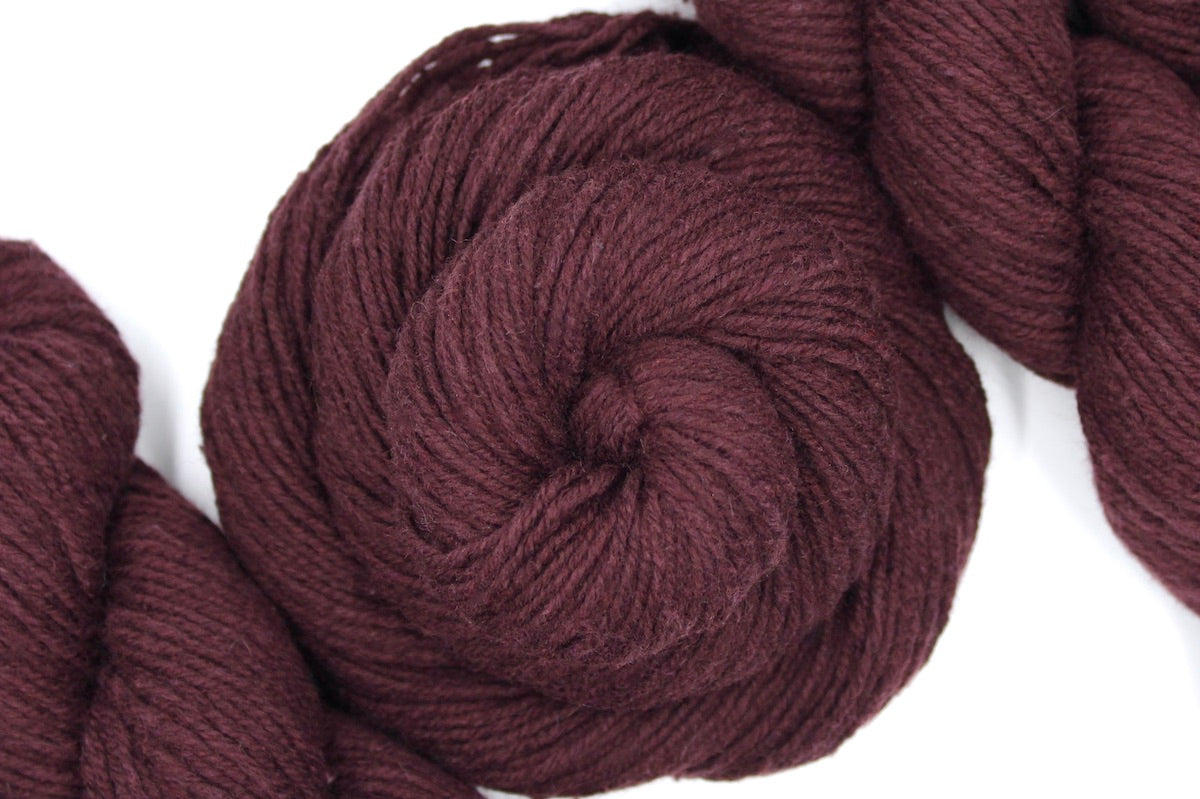 A skein of Vegan, Maroon/ Reddish Brown, Cotton/ Acrylic/ Nylon, Dk weight Yarn recycled by hand from unwanted sweaters swirled attractively in the center of the frame.