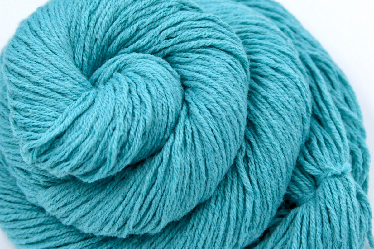 A close up shot of a skein of Vegan, Robin’s Egg Blue, Cotton/ Acrylic, Sport weight Yarn recycled by hand from unwanted sweaters beautifully coiled in the center of the frame.