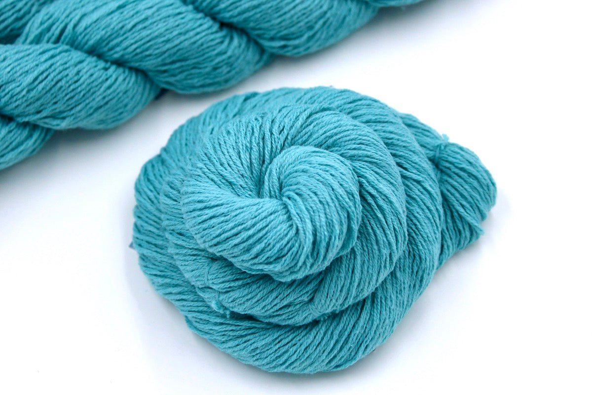 A skein of Vegan, Robin’s Egg Blue, Cotton/ Acrylic, Sport weight Yarn recycled by hand from unwanted sweaters swirled attractively in the center of the frame.