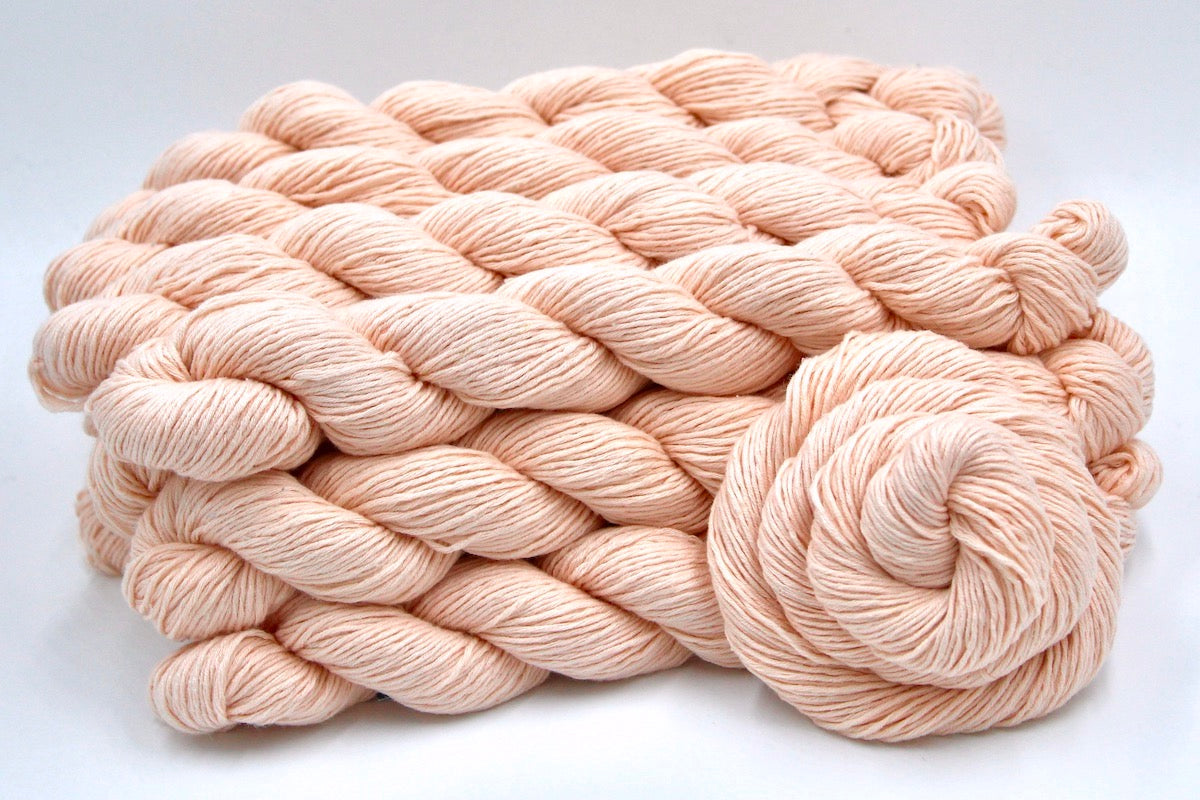 Several skeins of Vegan, Light Pastel Peach/ Pink, Cotton/ Rayon/ Nylon, Sport weight recycled by hand from unwanted sweaters stacked on top of each other attractively.