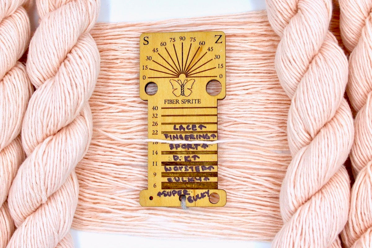 A skein of Vegan, Light Pastel Peach/ Pink, Cotton/ Rayon/ Nylon, Sport Weight Yarn recycled by hand from unwanted sweaters draped over a Llama shaped Yarn weight tool.