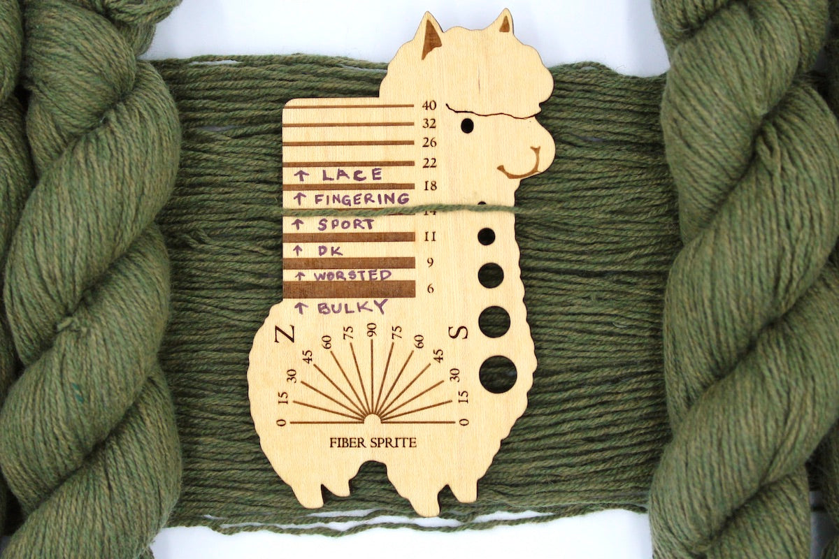 A skein of Heathered Sage, Olive Green, Cotton/ Nylon/ Wool, Sport Weight Yarn recycled by hand from unwanted sweaters draped over a Llama shaped Yarn weight tool.