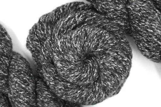 A skein of Heathered Charcoal Grey and White, Wool/ Acrylic/ Cotton/ Polyester, Heavy Worsted weight Yarn recycled by hand from unwanted sweaters swirled attractively in the center of the frame.