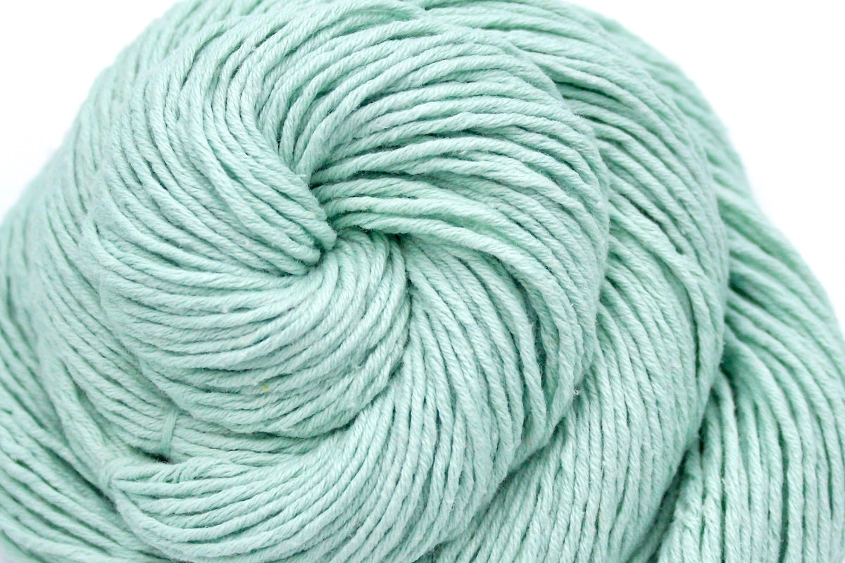 A close up shot of a skein of Vegan, Seafoam/ Aquamarine Blueish Green, 100% Cotton, Dk weight Yarn recycled by hand from unwanted sweaters beautifully coiled in the center of the frame.