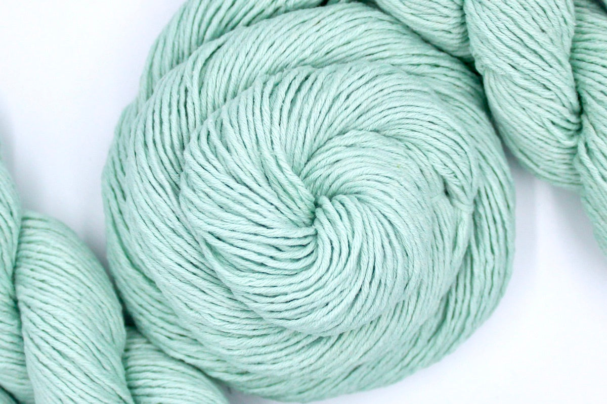A skein of Vegan, Seafoam/ Aquamarine Blueish Green, 100% Cotton, Dk weight Yarn recycled by hand from unwanted sweaters swirled attractively in the center of the frame.