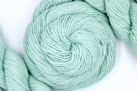 A skein of Vegan, Seafoam/ Aquamarine Blueish Green, 100% Cotton, Dk weight Yarn recycled by hand from unwanted sweaters swirled attractively in the center of the frame.