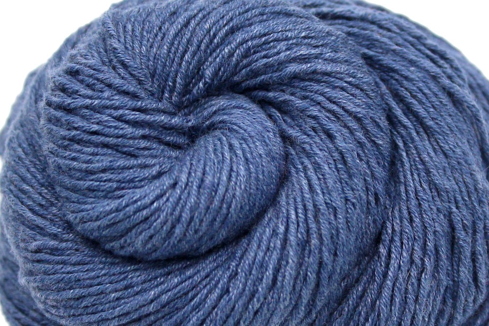 A close up shot of a skein of Vegan, Heathered Slate Grayish Blue, Cotton/ Acrylic, Sport weight Yarn recycled by hand from unwanted sweaters beautifully coiled in the center of the frame.