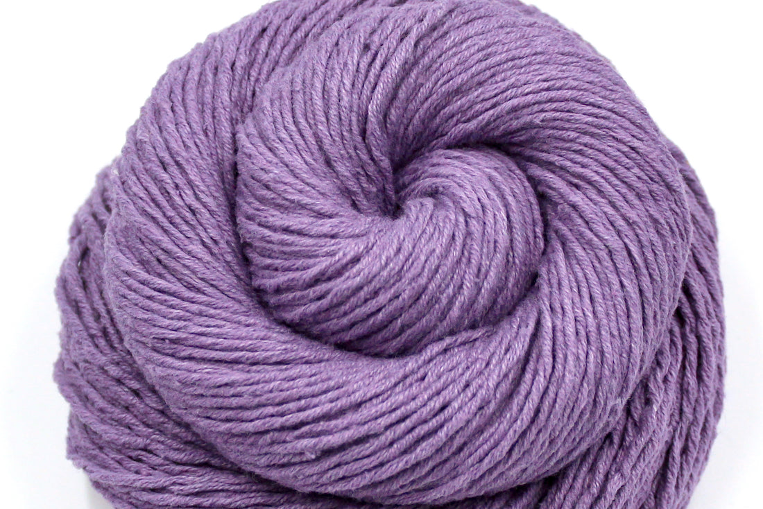 A close up shot of a skein of Vegan, Dusky Lavender, 60% Cotton, 40% Acrylic, DK weight Yarn recycled by hand from unwanted sweaters beautifully coiled in the center of the frame.