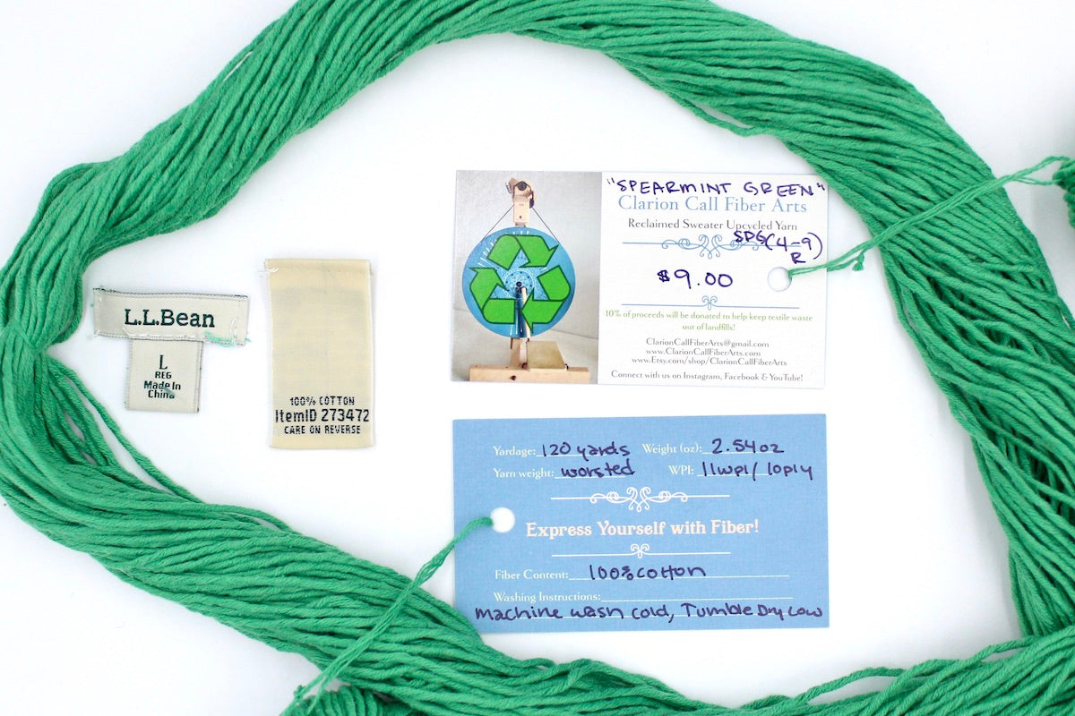 A skein of Vegan, Bright Spearmint Green, 100% Cotton, Worsted Weight yarn encircling the sweater labels it was recycled from, as well as the hand written yarn tags detailing the specs of this upcycled yarn to help you make your next project!