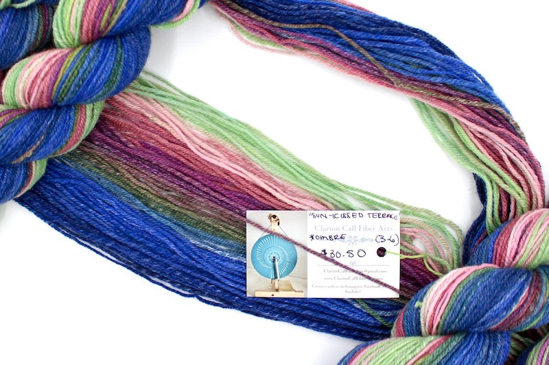 A one of a kind, hand dyed gradient skein of multicolored Navy Blue, Royal Blue, Teal, Green, Olive Green, Magenta, Salmon, Pastel Pink and Mint Green self-striping wool Yarn draped diagonally across the frame, so you can really see the color play.