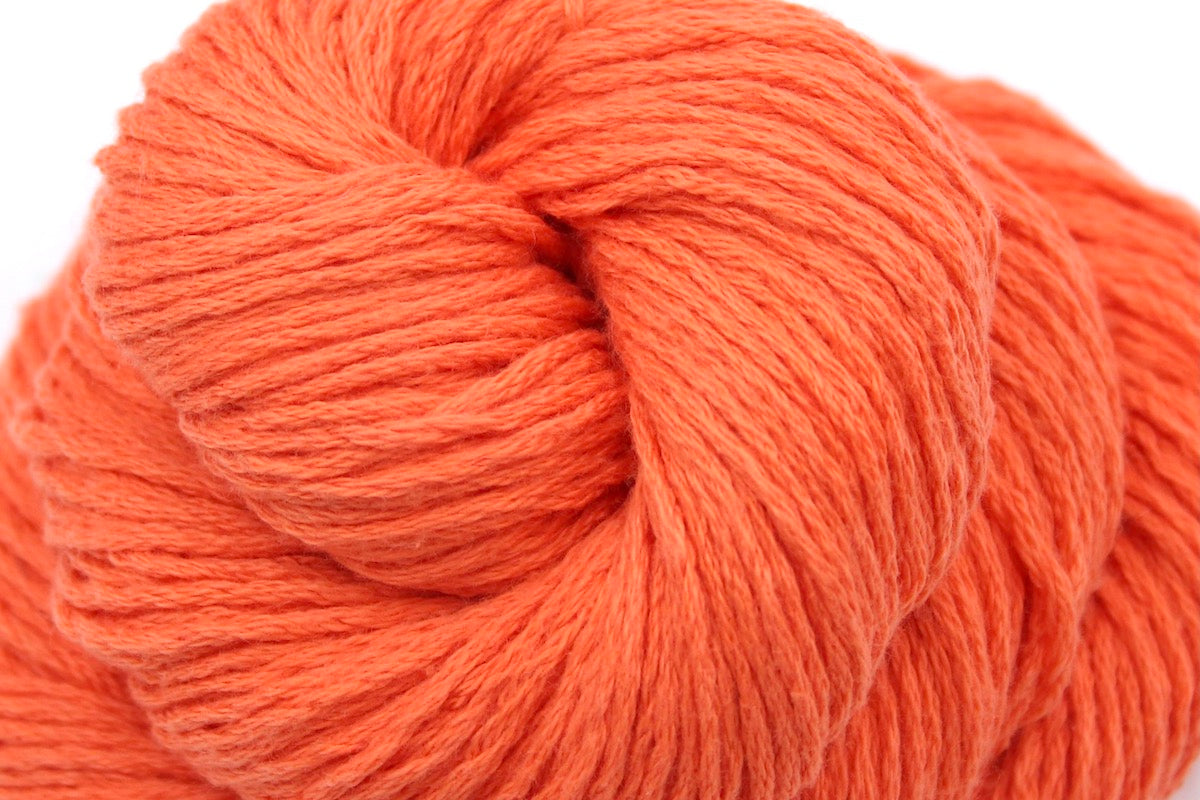 A close up shot of a skein of Vegan, Neon Tangerine Orange, Cotton/ Nylon, Dk weight Yarn recycled by hand from unwanted sweaters beautifully coiled in the center of the frame.