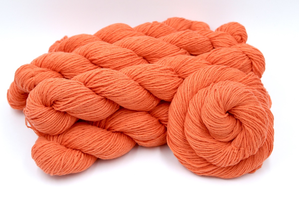 Several skeins of Vegan, Neon Tangerine Orange, Cotton/ Nylon, Dk weight recycled by hand from unwanted sweaters stacked on top of each other attractively.