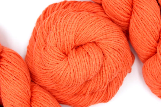 A skein of Vegan, Neon Tangerine Orange, Cotton/ Nylon, Dk weight Yarn recycled by hand from unwanted sweaters swirled attractively in the center of the frame.