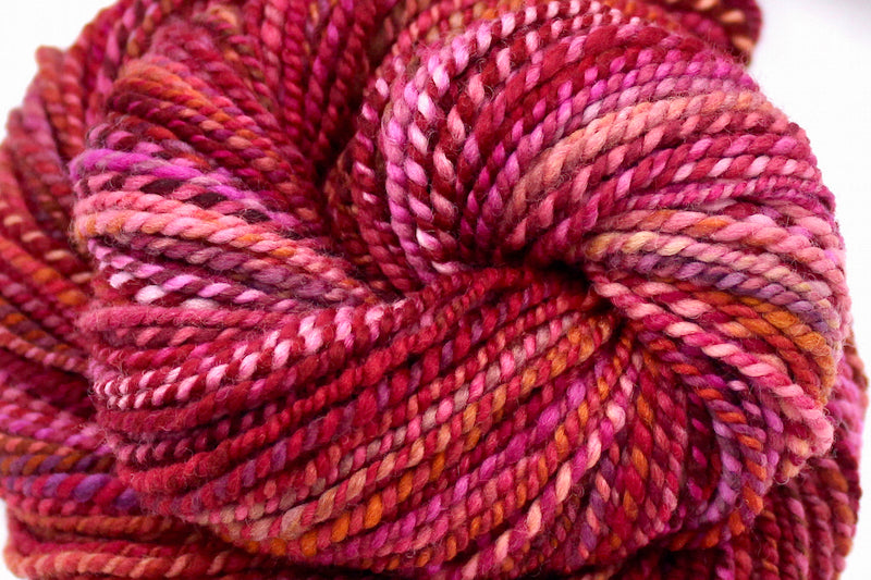 A close up view of a one of a kind, hand dyed variegated skein of multicolored Red, Pink, and Orange self-striping wool Yarn.