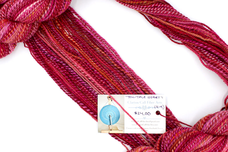 A one of a kind, hand dyed variegated skein of multicolored Red, Pink, and Orange self-striping wool Yarn draped diagonally across the frame, so you can really see the color play.