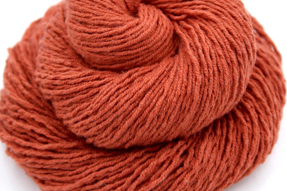 A close up shot of a skein of Vegan, Rusty Red/ Terracotta Orange, Cotton/ Acrylic, Fingering weight Yarn recycled by hand from unwanted sweaters beautifully coiled in the center of the frame.
