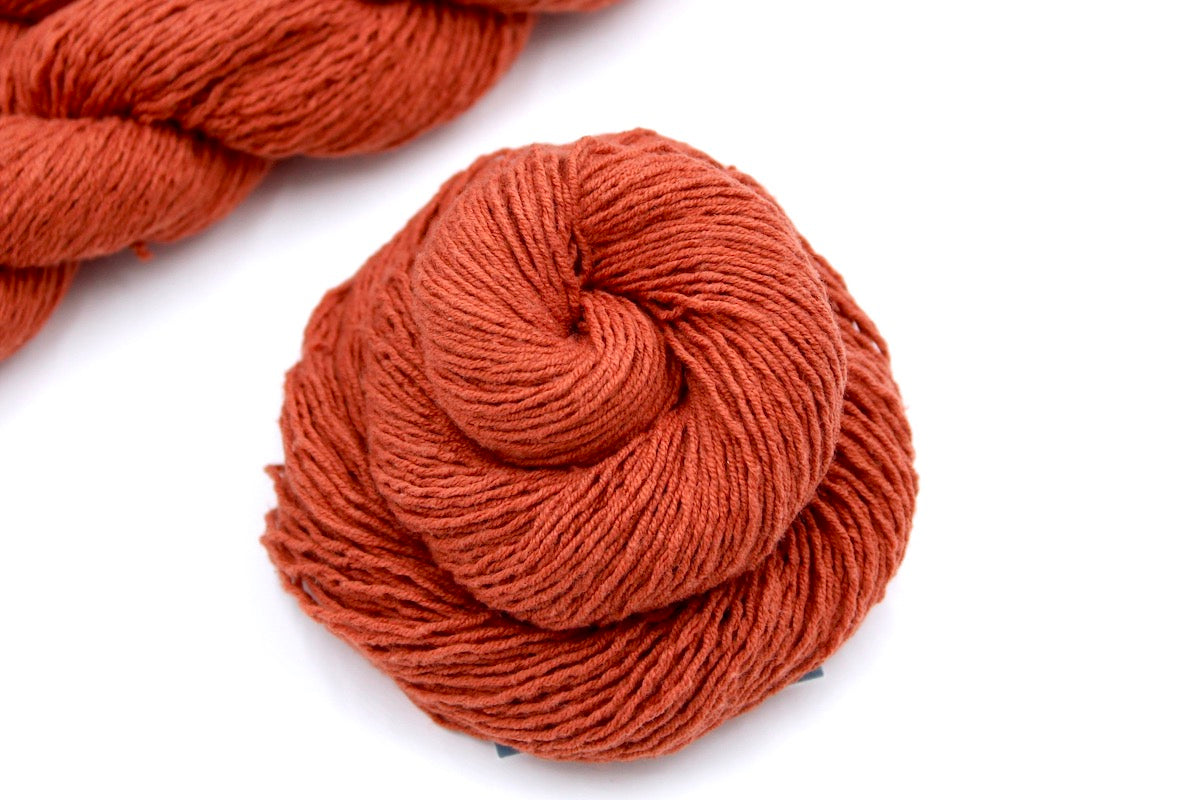 A skein of Vegan, Rusty Red/ Terracotta Orange, Cotton/ Acrylic, Fingering weight Yarn recycled by hand from unwanted sweaters swirled attractively in the center of the frame.