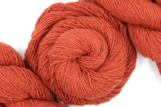 A skein of Vegan, Rusty Red/ Terracotta Orange, Cotton/ Acrylic, Fingering weight Yarn recycled by hand from unwanted sweaters swirled attractively in the center of the frame.