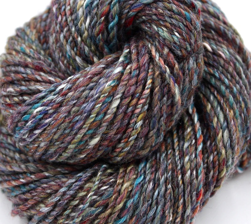 A close up view of a one of a kind, hand dyed variegated skein of multicolored Maroon, Red, Grey, Blue, Yellow, and Brown self-striping wool Yarn.