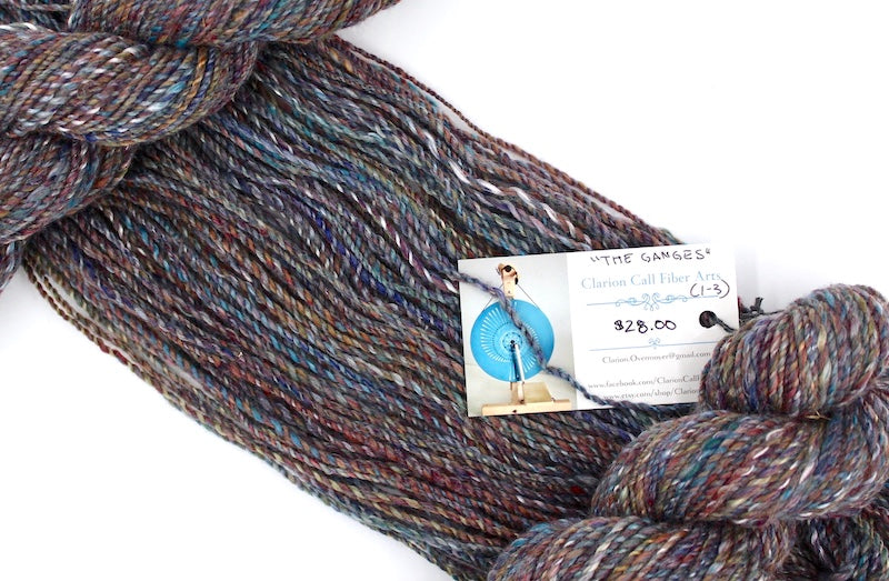 A one of a kind, hand dyed variegated skein of multicolored Maroon, Red, Grey, Blue, Yellow, and Brown self-striping wool Yarn draped diagonally across the frame, so you can really see the color play.