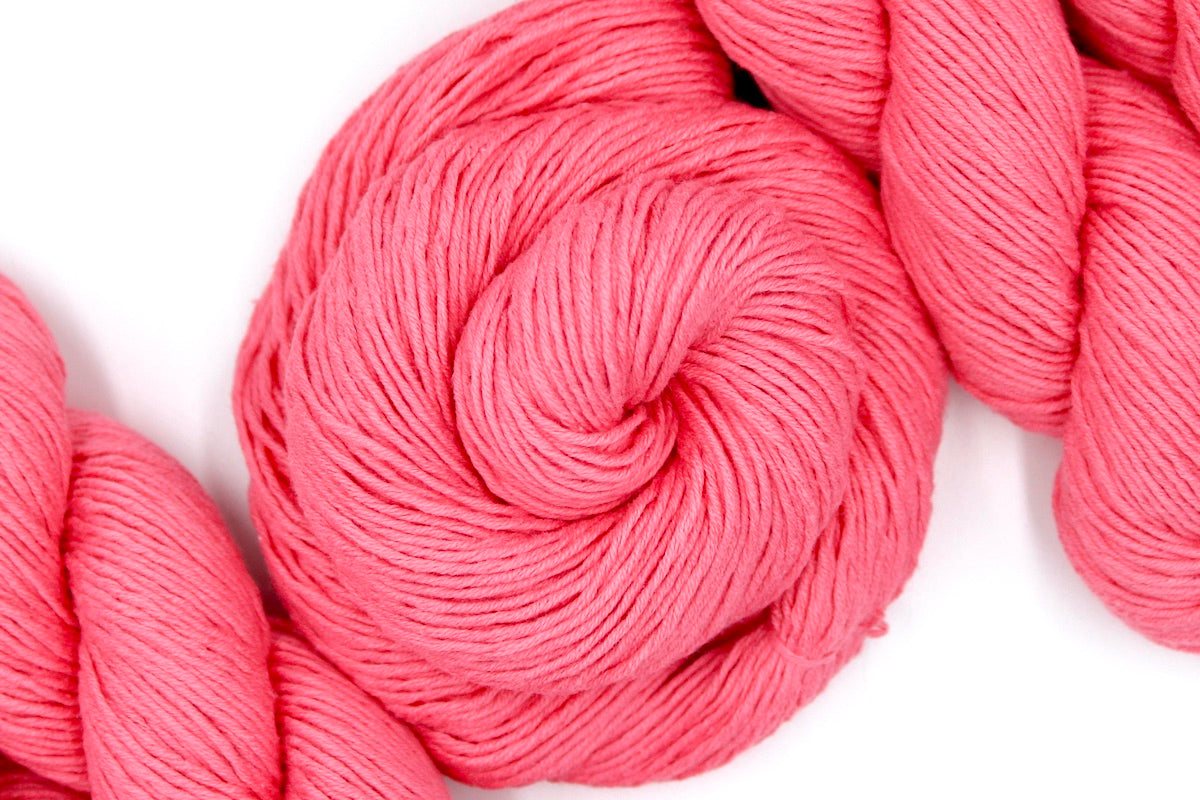 A skein of Vegan, Neon Rose Pink/ Fuchsia, 100% Cotton, Sport weight Yarn recycled by hand from unwanted sweaters swirled attractively in the center of the frame.