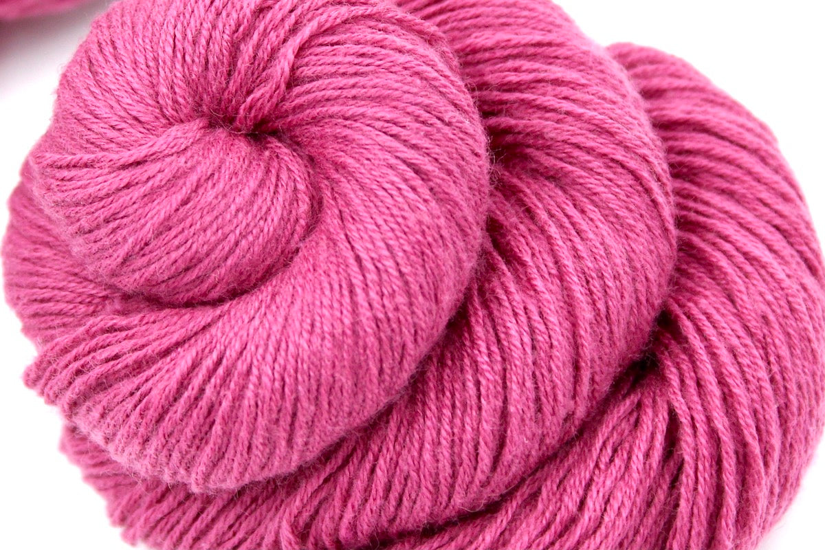 A close up shot of a skein of Vegan, Watermelon Fuchsia/ Rose Pink, Cotton/ Rayon/ Nylon, Fingering weight Yarn recycled by hand from unwanted sweaters beautifully coiled in the center of the frame.