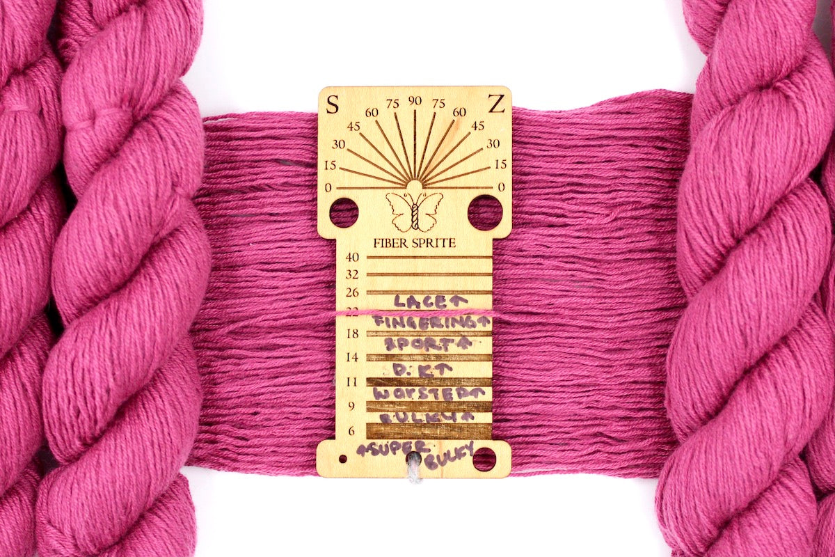 A skein of Vegan, Watermelon Fuchsia/ Rose Pink, Cotton/ Rayon/ Nylon, Fingering Weight Yarn recycled by hand from unwanted sweaters draped over a Llama shaped Yarn weight tool.