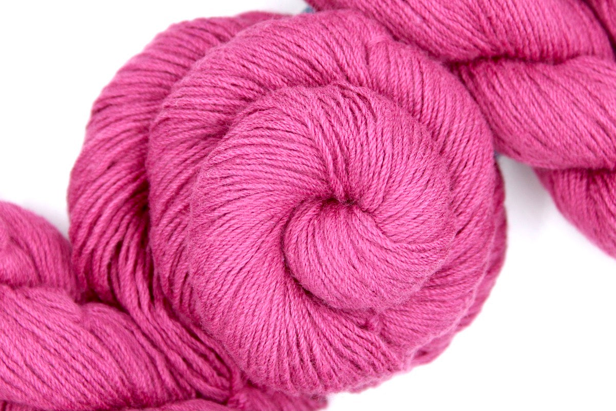 A skein of Vegan, Watermelon Fuchsia/ Rose Pink, Cotton/ Rayon/ Nylon, Fingering weight Yarn recycled by hand from unwanted sweaters swirled attractively in the center of the frame.