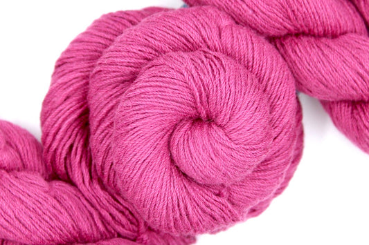 A skein of Vegan, Watermelon Fuchsia/ Rose Pink, Cotton/ Rayon/ Nylon, Fingering weight Yarn recycled by hand from unwanted sweaters swirled attractively in the center of the frame.