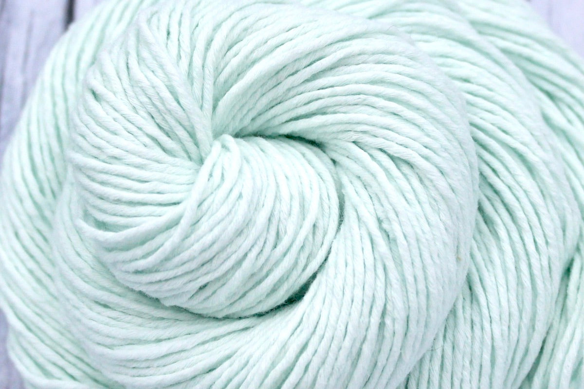 A close up shot of a skein of Vegan, Light Pastel Mint Green, 100% Cotton, Sport weight Yarn recycled by hand from unwanted sweaters beautifully coiled in the center of the frame.