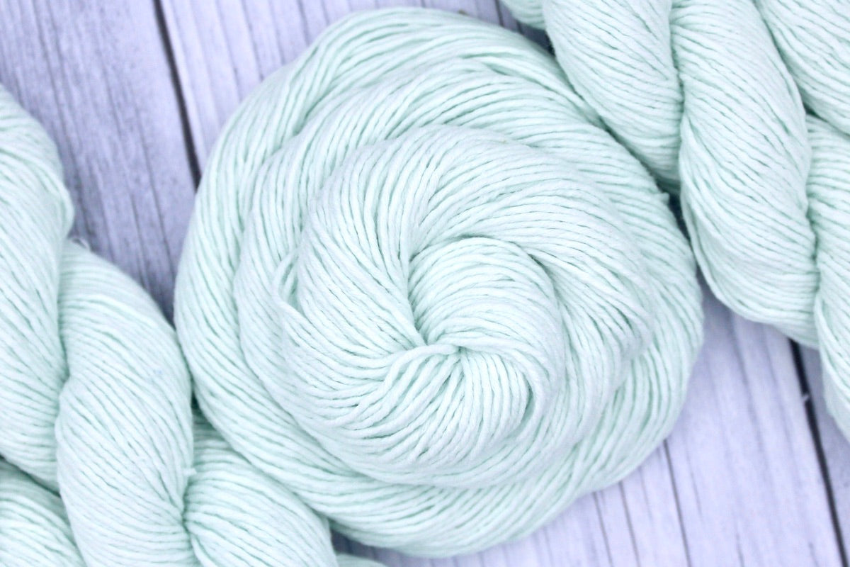 A skein of Vegan, Light Pastel Mint Green, 100% Cotton, Sport weight Yarn recycled by hand from unwanted sweaters swirled attractively in the center of the frame.