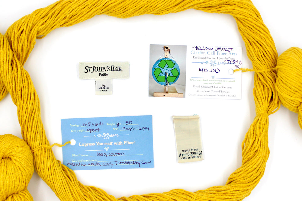A skein of Vegan, Mustard Yellow, 100% Cotton, Sport Weight yarn encircling the sweater labels it was recycled from, as well as the hand written yarn tags detailing the specs of this recycled yarn to help you make your next project!