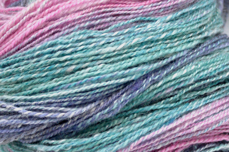 A close up view of a one of a kind, hand dyed gradient skein of multicolored Light Pink, Sky Blue, Seafoam Green, Grey, and Lavender self-striping wool Yarn. 