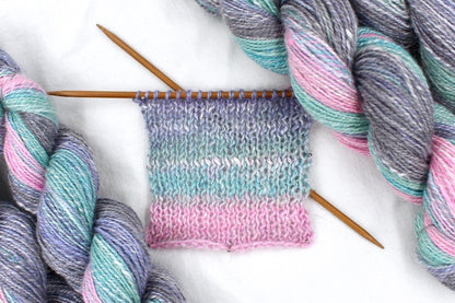 A sample swatch knitted from a one of a kind, hand dyed gradient skein of multicolored Light Pink, Sky Blue, Seafoam Green, Grey, and Lavender self-striping wool Yarn. 