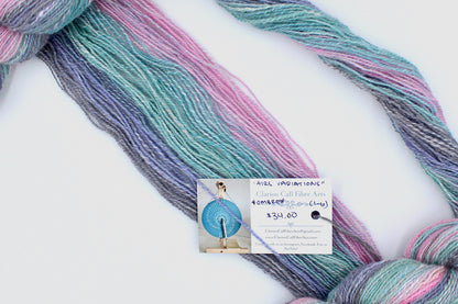 A one of a kind, hand dyed gradient skein of gradient skein of multicolored Light Pink, Sky Blue, Seafoam Green, Grey, and Lavender self-striping wool Yarn draped diagonally across the frame, so you can really see the color play. 