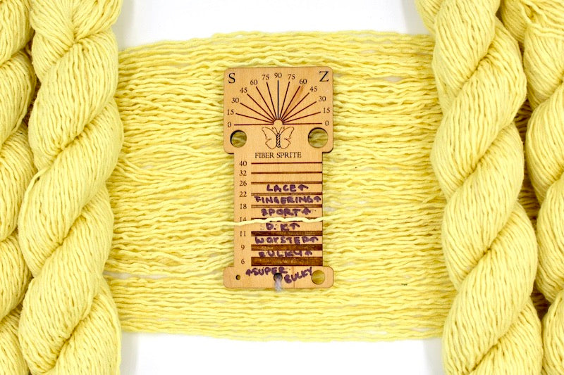 A skein of dk weight Bright Yellow Yarn recycled by hand from unwanted sweaters draped over a Yarn weight tool 