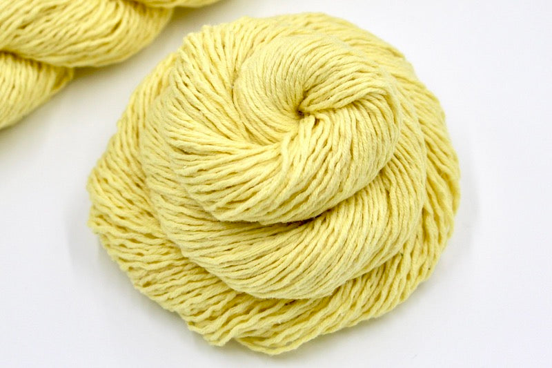 A close up shot of a skein of Bright Yellow Yarn recycled by hand from unwanted sweaters beautifully coiled in the center of the frame