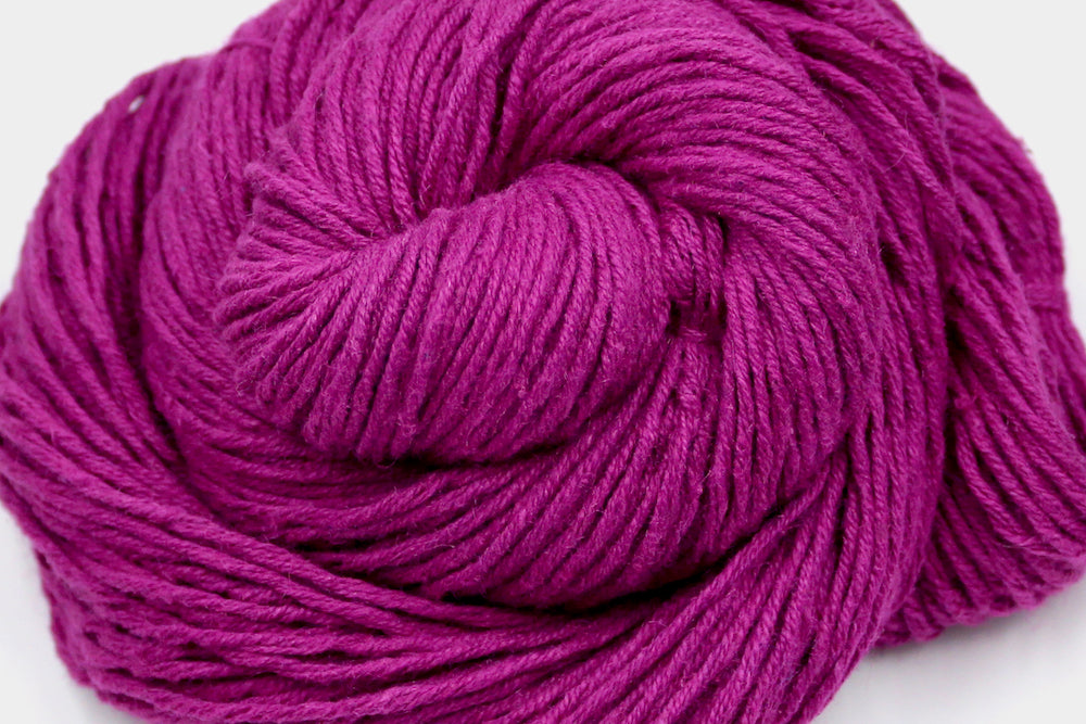 A close up shot of a skein of Vegan, Bright Fuchsia Pink, 55% Ramie, 45% Cotton, Worsted weight Yarn recycled by hand from unwanted sweaters beautifully coiled in the center of the frame. 