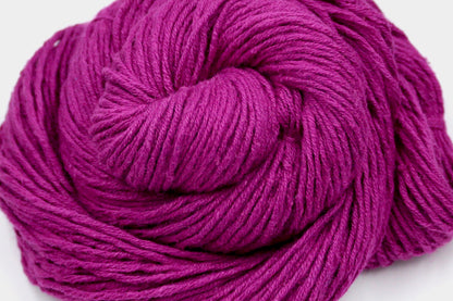 A close up shot of a skein of Vegan, Bright Fuchsia Pink, 55% Ramie, 45% Cotton, Worsted weight Yarn recycled by hand from unwanted sweaters beautifully coiled in the center of the frame. 