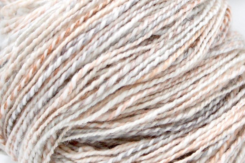A close up view of a one of a kind, hand dyed g variegated skein of multicolored Cream, Dusky Pink, and Grey self-striping wool Yarn. 