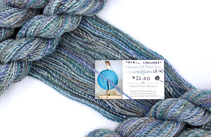 A one of a kind, hand dyed variegated skein of multicolored Navy, Teal, Royal Blue, Lavender, and Tan self-striping wool Yarn draped diagonally across the frame, so you can really see the color play. 